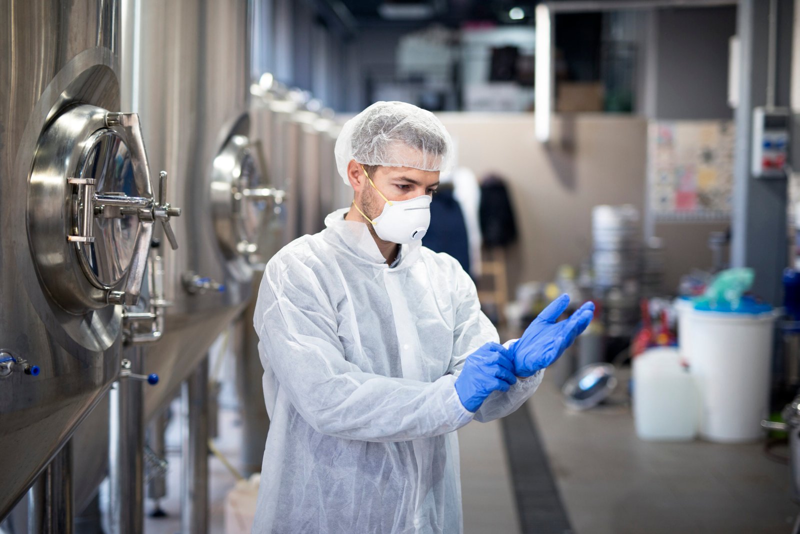 Young technologist putting on protective rubber gloves in production factory.